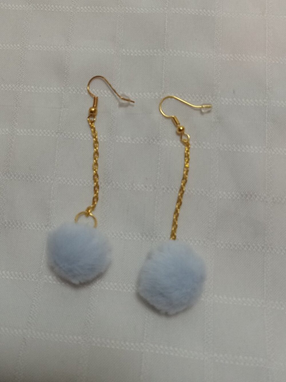 Handmade earrings with small pom-poms and gold-colored accent hooks and chains